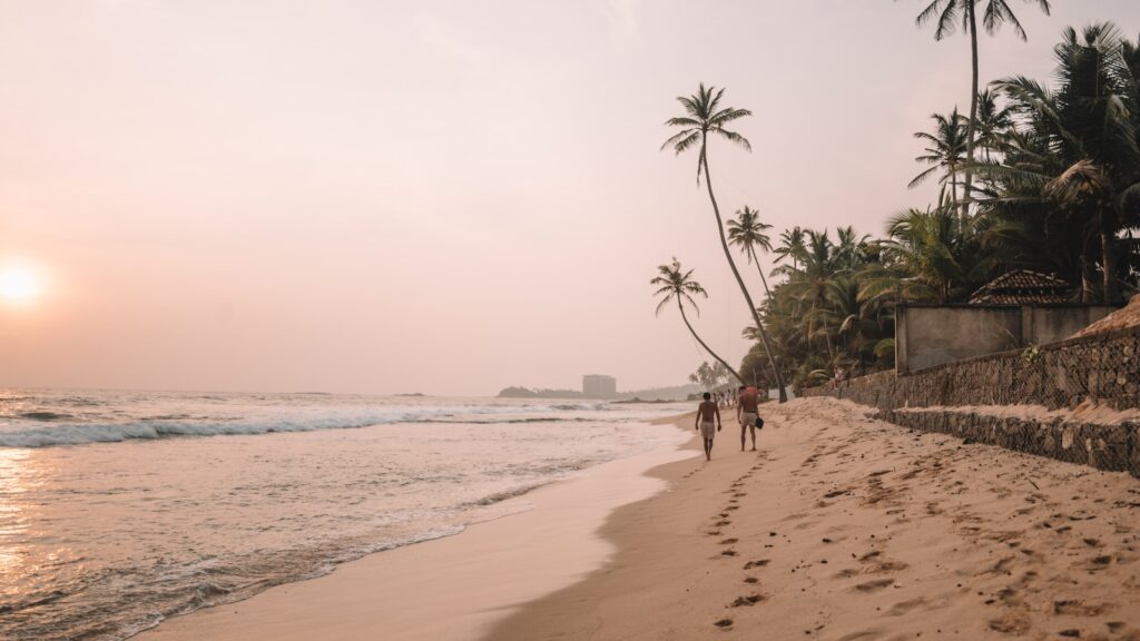 a couple of people walking down a beach next to the ocean